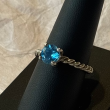 Load image into Gallery viewer, Ring with a blue gemstone on a black stand against a beige background
